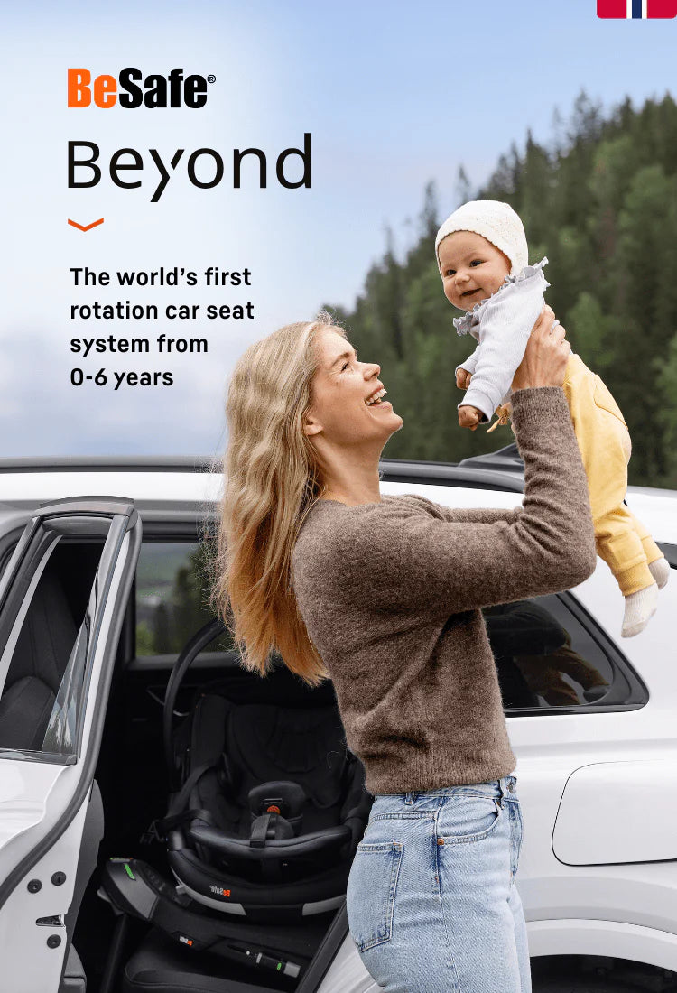 Woman holding a baby next to a car with a Besafe car seat, set against a forest background.