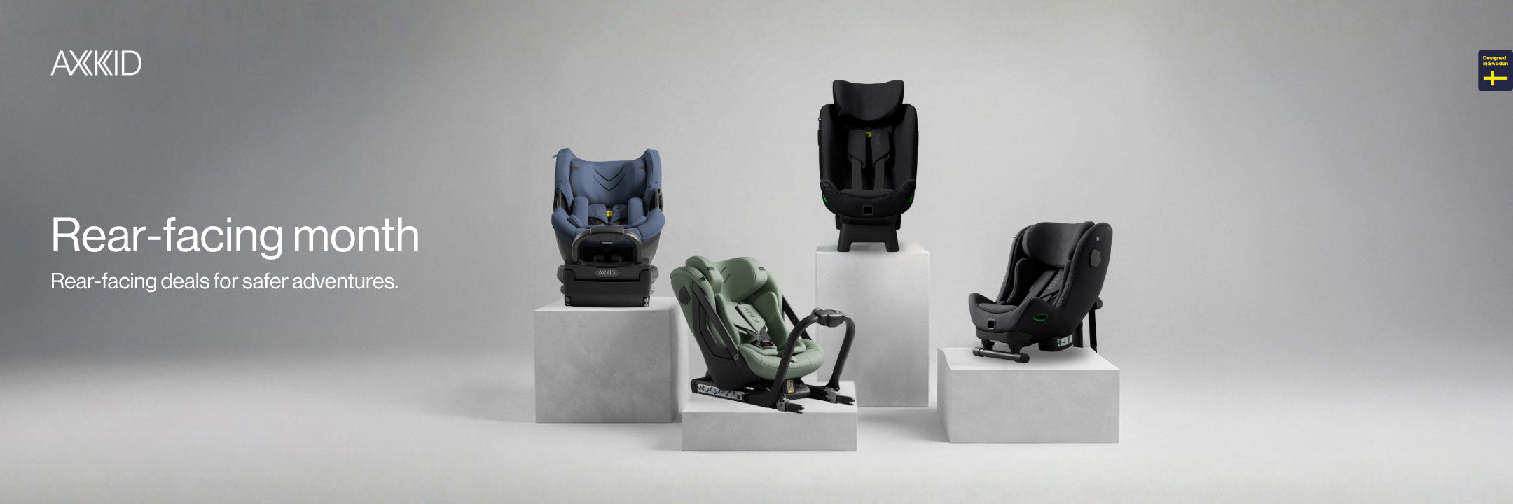 Baby car seats displayed on pedestals with AXKID branding and text about rear-facing month.